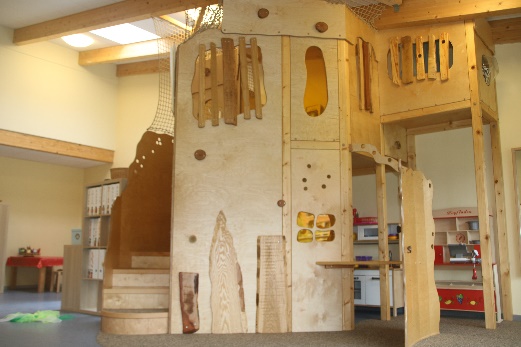 Ein Indoor-Klettergerüst aus naturbelassenem Holz. Es gibt einige Versteckmöglichkeiten, das Gerüst erinnert an ein Baumhaus.